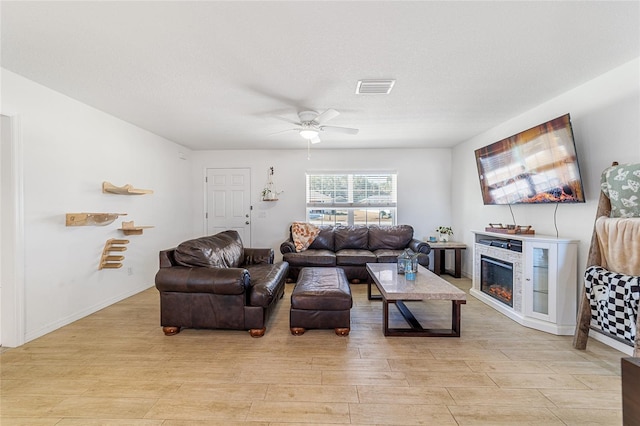 living room with a stone fireplace, ceiling fan, light hardwood / wood-style flooring, and a textured ceiling