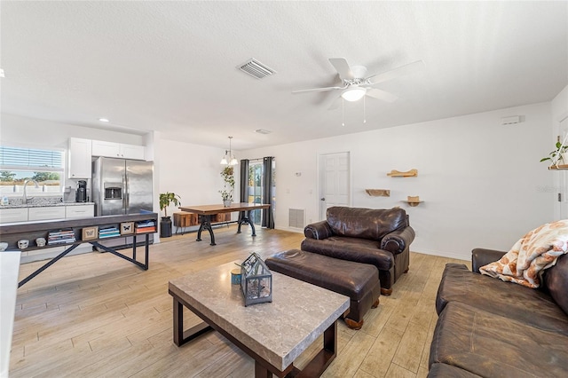 living room featuring a textured ceiling, ceiling fan with notable chandelier, sink, and light hardwood / wood-style flooring