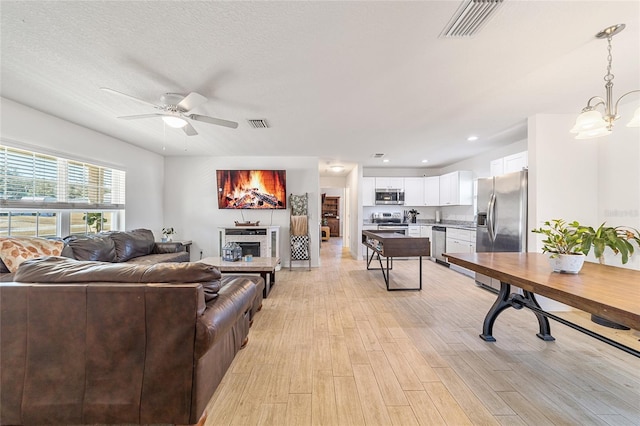 living room featuring a textured ceiling, light hardwood / wood-style floors, and ceiling fan with notable chandelier