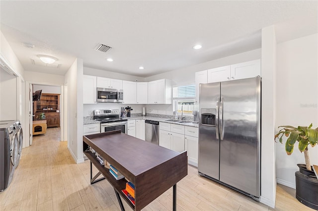 kitchen featuring white cabinets, washing machine and dryer, stainless steel appliances, and light hardwood / wood-style flooring