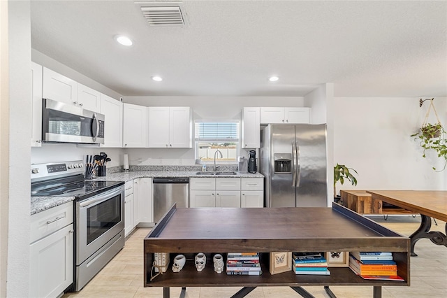 kitchen with sink, a textured ceiling, light stone counters, white cabinetry, and stainless steel appliances