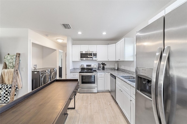 kitchen with white cabinetry, washing machine and dryer, light stone counters, light hardwood / wood-style flooring, and appliances with stainless steel finishes