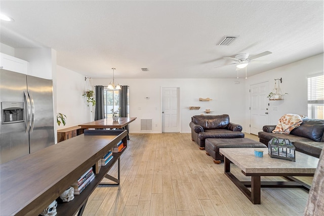 living room with ceiling fan with notable chandelier, a textured ceiling, and light hardwood / wood-style flooring