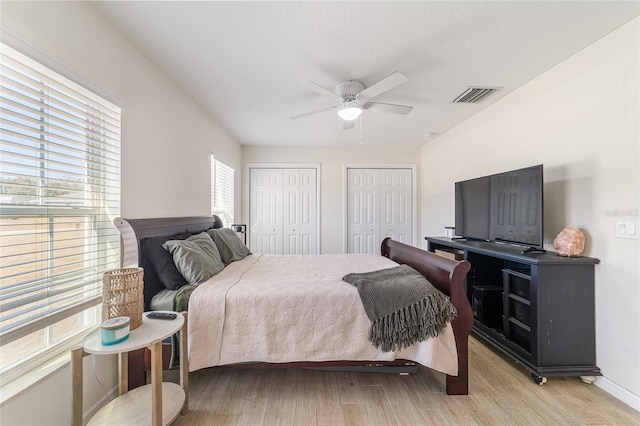 bedroom with ceiling fan, light hardwood / wood-style floors, and two closets