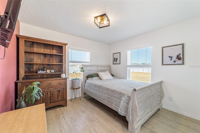 bedroom featuring multiple windows, light hardwood / wood-style floors, and a textured ceiling