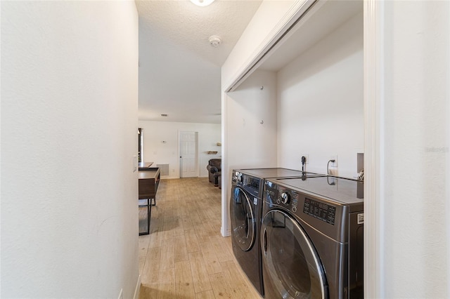 clothes washing area with separate washer and dryer, a textured ceiling, and light hardwood / wood-style floors