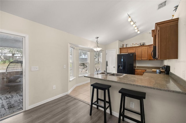 kitchen featuring kitchen peninsula, black refrigerator with ice dispenser, a breakfast bar, sink, and decorative light fixtures