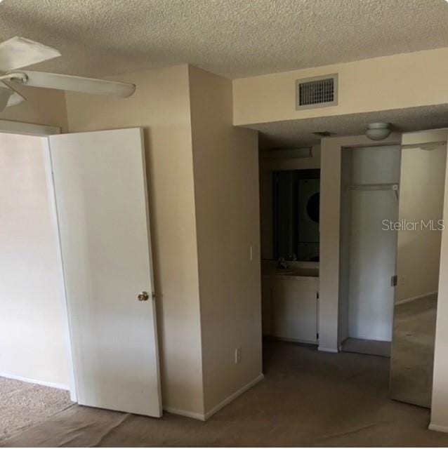 unfurnished bedroom with stacked washer / dryer, ceiling fan, and a textured ceiling