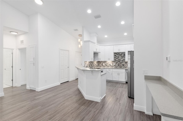 kitchen featuring backsplash, a high ceiling, stainless steel fridge, light hardwood / wood-style floors, and white cabinetry