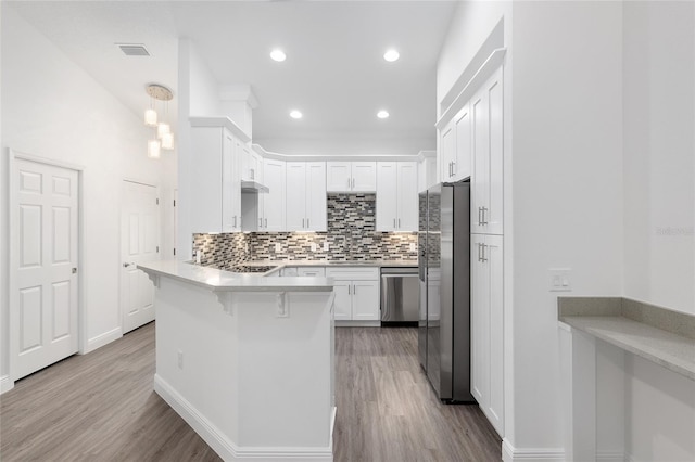 kitchen with white cabinetry, appliances with stainless steel finishes, light hardwood / wood-style floors, kitchen peninsula, and a breakfast bar area