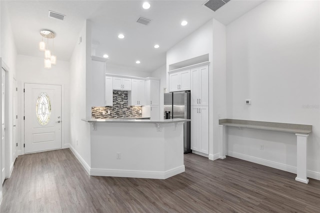 kitchen featuring a kitchen breakfast bar, dark hardwood / wood-style floors, stainless steel refrigerator with ice dispenser, kitchen peninsula, and white cabinets