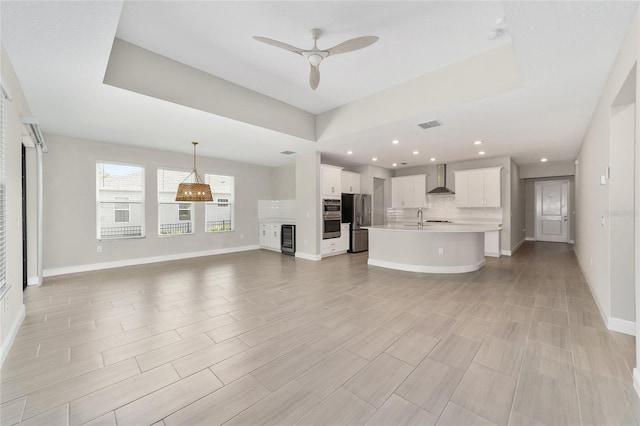 kitchen with light hardwood / wood-style flooring, wall chimney exhaust hood, an island with sink, white cabinetry, and stainless steel appliances