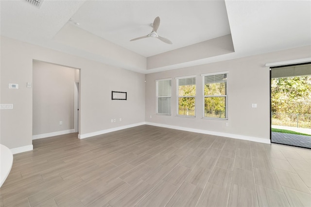 empty room featuring light wood-type flooring, a tray ceiling, and ceiling fan