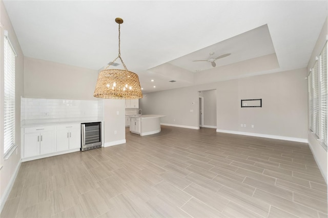 unfurnished living room featuring ceiling fan, sink, wine cooler, and a tray ceiling