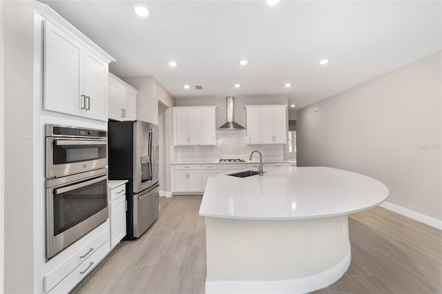 kitchen featuring white cabinets, stainless steel appliances, a kitchen island with sink, and wall chimney exhaust hood