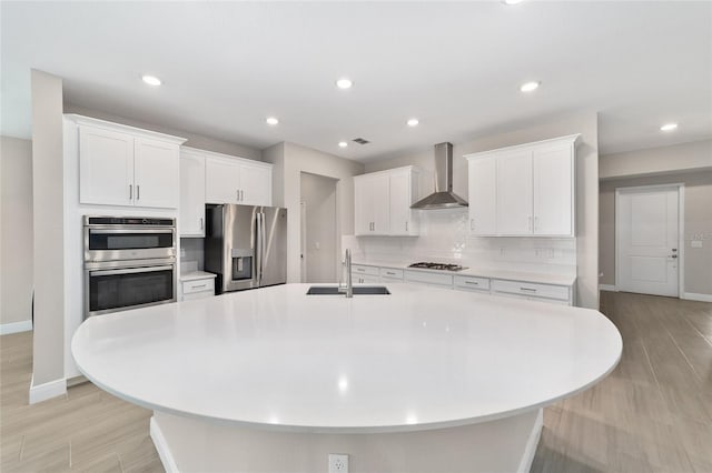 kitchen featuring wall chimney exhaust hood, white cabinetry, a large island with sink, and appliances with stainless steel finishes