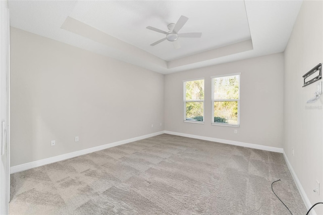 empty room with a raised ceiling, light carpet, and ceiling fan