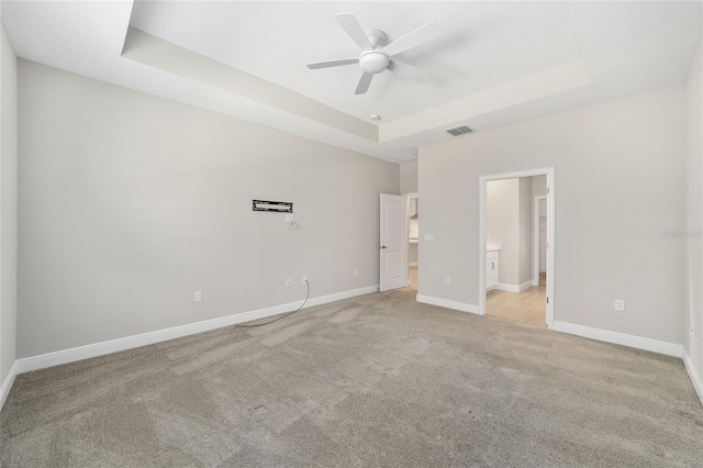 unfurnished bedroom with a raised ceiling, ensuite bath, ceiling fan, and light carpet