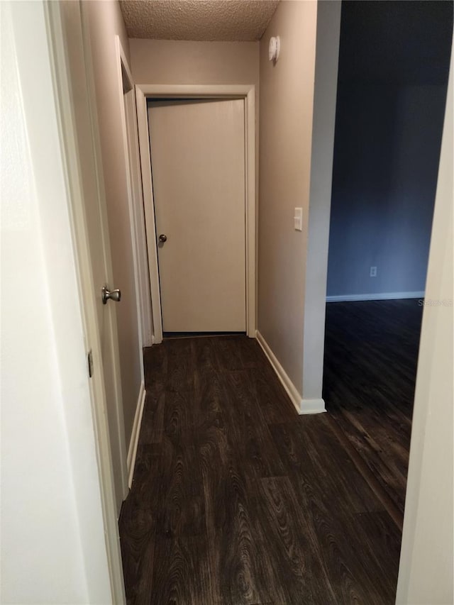 hallway with a textured ceiling and dark hardwood / wood-style floors