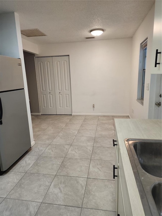 kitchen with a textured ceiling, sink, and stainless steel refrigerator