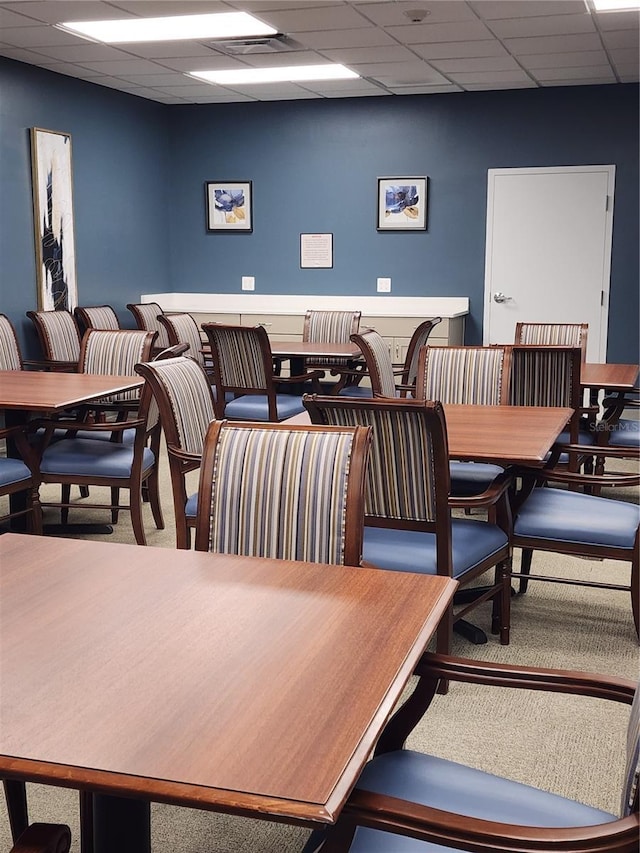 carpeted dining area with a drop ceiling