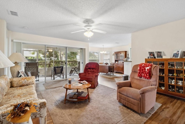 living room with ceiling fan with notable chandelier, wood-type flooring, and a textured ceiling