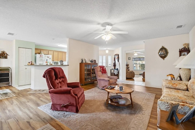 living room with ceiling fan, a textured ceiling, and light wood-type flooring