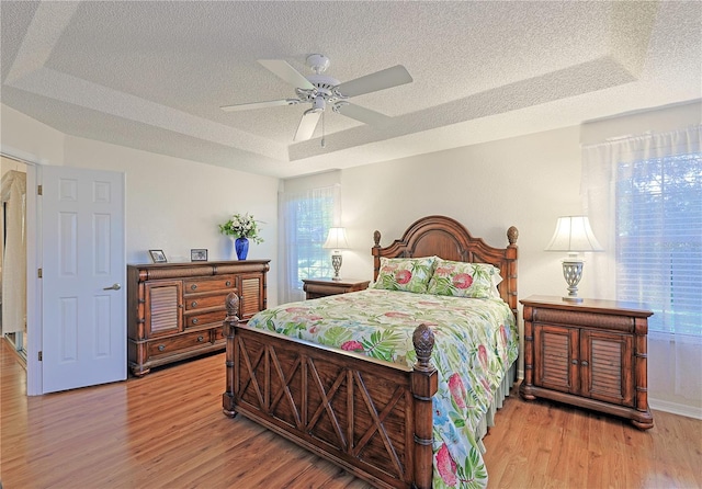 bedroom featuring a textured ceiling, ceiling fan, light hardwood / wood-style flooring, and a tray ceiling