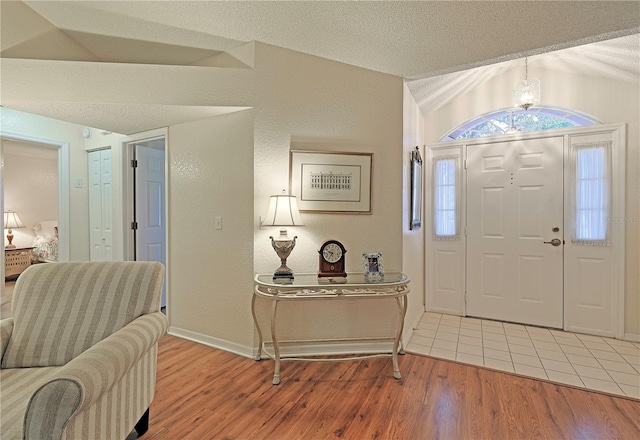 foyer entrance featuring a textured ceiling, wood-type flooring, and vaulted ceiling