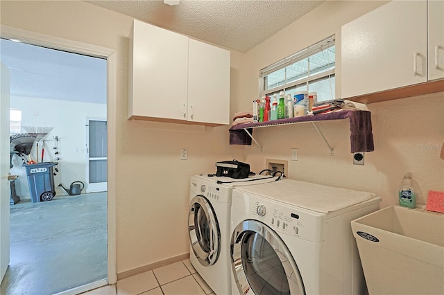 clothes washing area featuring washing machine and clothes dryer, sink, cabinets, a textured ceiling, and light tile patterned flooring