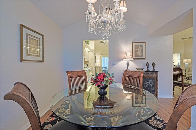 dining area featuring ceiling fan with notable chandelier, wood-type flooring, and vaulted ceiling