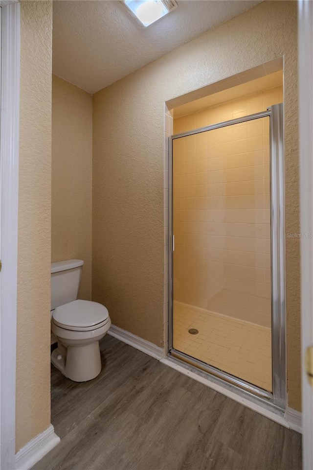 bathroom featuring a textured ceiling, hardwood / wood-style flooring, toilet, and a shower with door