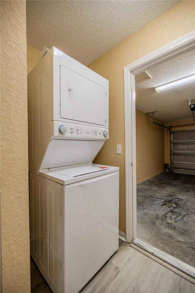 laundry area featuring light hardwood / wood-style flooring, stacked washing maching and dryer, and a textured ceiling