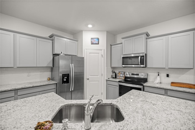 kitchen with decorative backsplash, sink, light stone counters, and appliances with stainless steel finishes