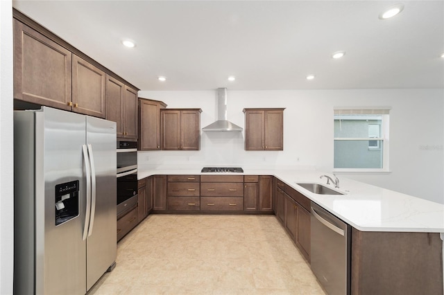 kitchen featuring kitchen peninsula, light stone countertops, stainless steel appliances, sink, and wall chimney range hood