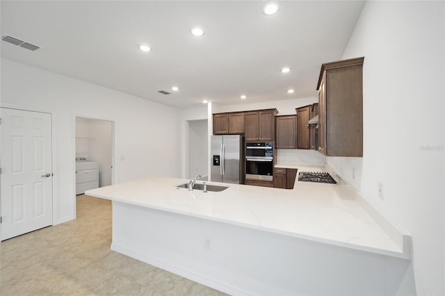 kitchen with kitchen peninsula, appliances with stainless steel finishes, light stone counters, sink, and washer / clothes dryer