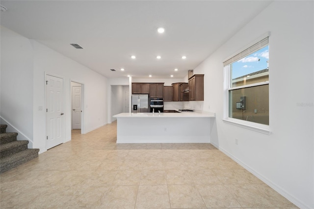 kitchen featuring kitchen peninsula, stainless steel refrigerator with ice dispenser, backsplash, dark brown cabinetry, and light tile patterned floors