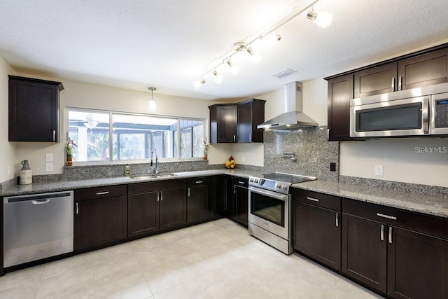 kitchen with dark brown cabinetry, sink, stainless steel appliances, and wall chimney range hood