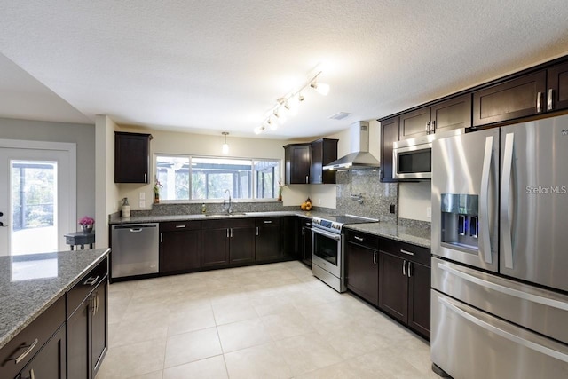 kitchen with light stone countertops, sink, wall chimney exhaust hood, dark brown cabinets, and appliances with stainless steel finishes