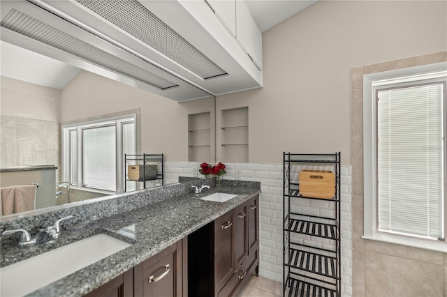 kitchen featuring built in shelves, dark brown cabinetry, sink, and dark stone counters