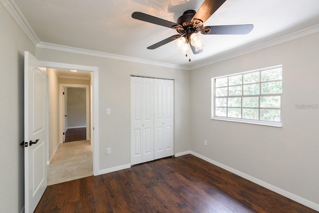 unfurnished bedroom featuring dark wood-type flooring, ceiling fan, a closet, and crown molding