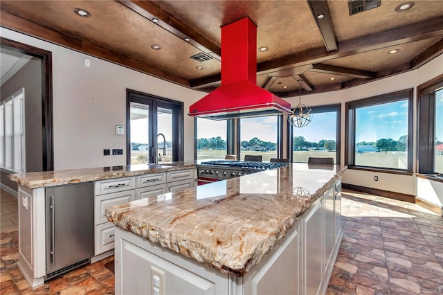 kitchen featuring light stone countertops, appliances with stainless steel finishes, a center island, white cabinetry, and beam ceiling