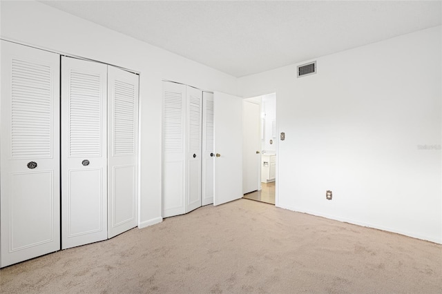 unfurnished bedroom with light colored carpet and two closets