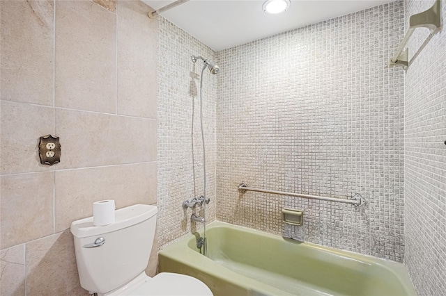 bathroom featuring tiled shower / bath, toilet, and tile walls