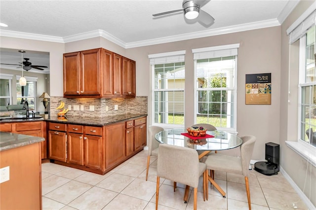 kitchen with light tile patterned floors, ornamental molding, sink, and dark stone countertops