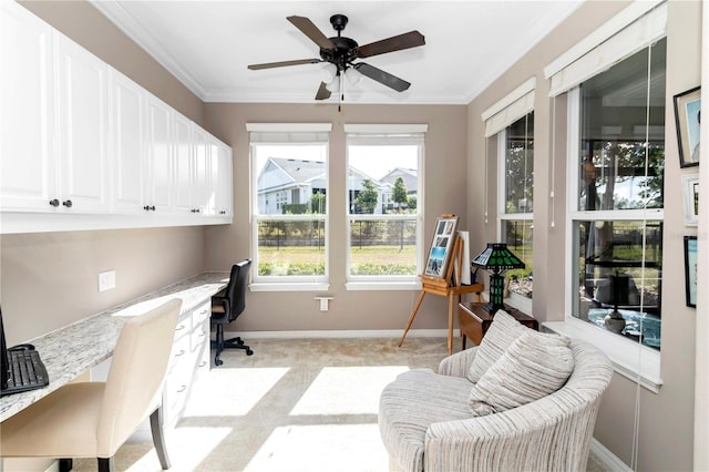 carpeted home office featuring ornamental molding, built in desk, and ceiling fan