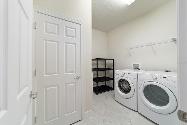 clothes washing area with a textured ceiling, separate washer and dryer, and light tile patterned flooring