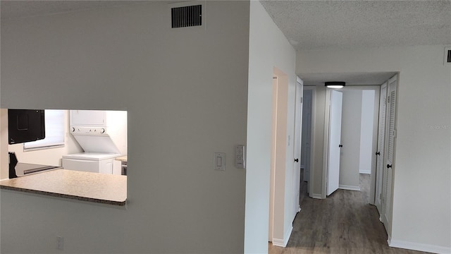 corridor with hardwood / wood-style flooring, a textured ceiling, and stacked washer and clothes dryer