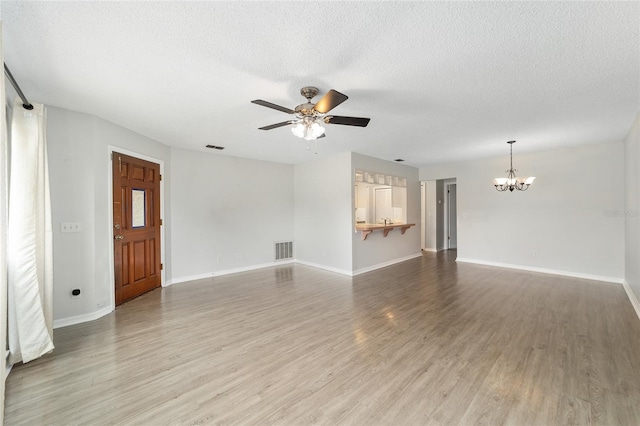 unfurnished living room with hardwood / wood-style floors, ceiling fan with notable chandelier, and a textured ceiling