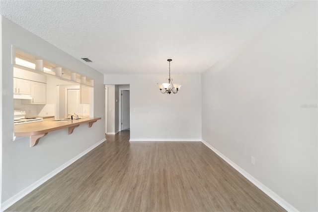 unfurnished dining area with sink, dark hardwood / wood-style flooring, a textured ceiling, and a notable chandelier